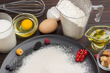 Ingredients for baking berry pie. Berries, flour in black plate. Measuring cup with flour, glass of milk, broken egg.