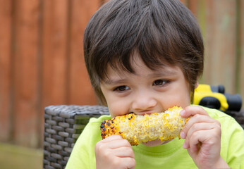 Head shot of  hungry little boy eating grilled sweet corn, Kid boy enjoy eating picnic food in thr garden in sunny day on summer, Healthy food for children concept