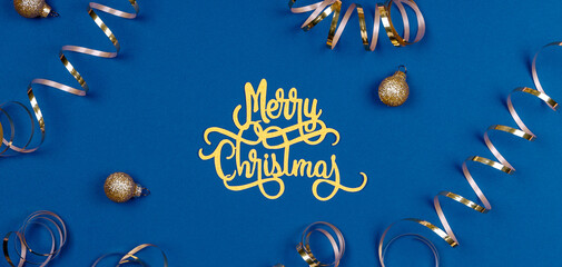 Holiday background with Merry Christmas wording, golden balls, and ribbons on classic blue. Holiday celebration card concept in banner format