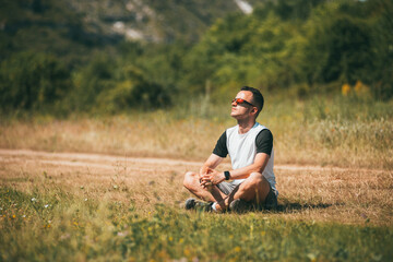 Naklejka na ściany i meble Young man is meditating on green grass in a field with face raised up to sky and eyes closed on sunny summer day