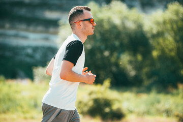 Young man is running outdoors in a field while wearing sunglasses