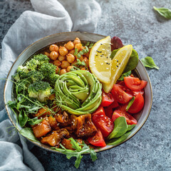 Buddha bowl salad with baked sweet potatoes, chickpeas, broccoli, tomatoes, greens, avocado, pea sprouts on light blue background with napkin. Healthy vegan food, clean eating, dieting, closeup