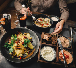 Dinner for two, fries potatoes with forest mushrooms, dumplings with herbs and berries and aperitif with rye bread on dark background. Woman eating dish with fork. Selective focus, stylized