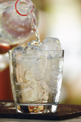 Clean water is poured from a bottle into a glass with ice. Close up