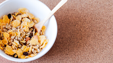 Plano cenital de un bowl blanco con cereales dentro junto a una cuchara de madera sobre un mantel...