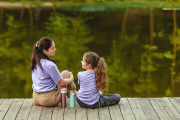 Happy family, mother and daughter resting in the park near the lake.