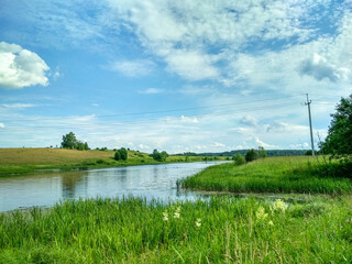Obraz premium Green summer meadow and river with blue cloudy sky