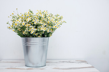 a bouquet of daisies flowers stands in a vase in the shape of a metal bucket on a white background