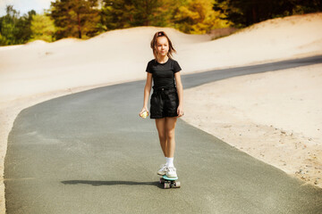 Walk on a skateboard. Teenage girl eats an apple and rides on a skateboard