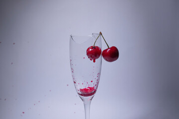 drops of red liquid - blood - in a broken champagne glass with a cherry on it on a white background. Isolated. Copy space. pain concept. High quality photo