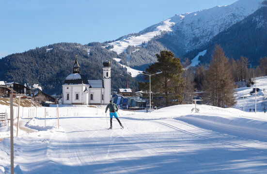 Cross-country skier on sunny track towards pitoresque church, Seefeld, Austria