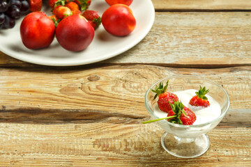 Strawberries in a cup with whipped cream on a table near fruits.