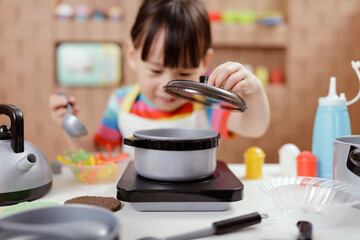 toddler girl pretend play food preparing role against cardboard blocks kitchen background