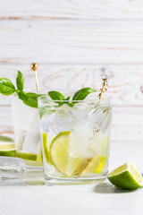 Refreshing homemade lemonade with line and basil on rustic wooden table close up. Summer cold drink on the table.