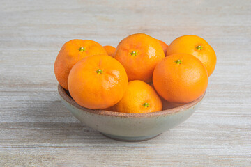 Fresh Oranges In A Ceramic Bowl Set On Wood Panel