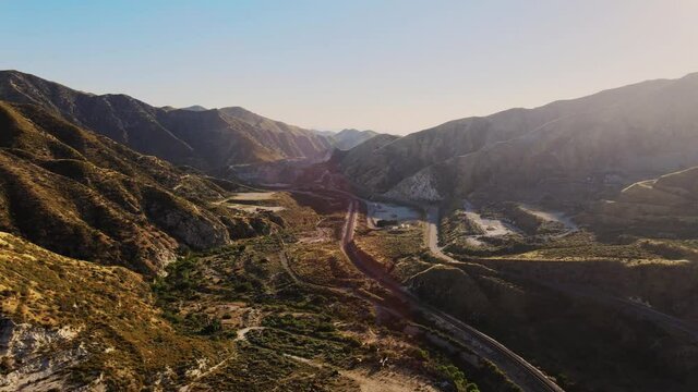 Drone shot with flare of a beautiful valley with train tracks at sunset