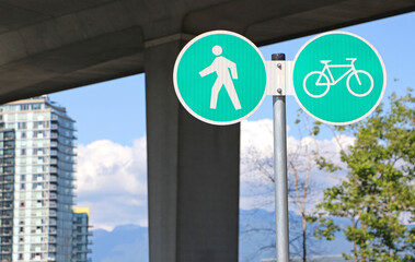 The street sign for pedestrians and bikers to separate / divide their pathways. The view on the light green signs with pedestrian and bike symbols. The building, tree and bridge in the background.