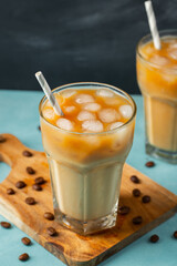 Ice coffee in a tall glass with cream poured over and coffee beans on a light stone background. Cold summer drink with tubes