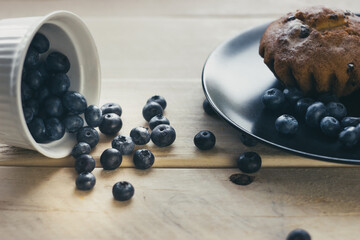 Blueberry muffins with powdered sugar and fresh berry. Fresh blueberries are scattered on the wooden table