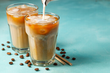 Ice coffee in a tall glass with cream poured over and coffee beans on a light stone background....