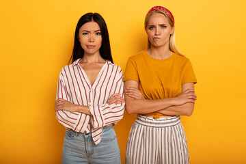 Two girl with troubled expression are diffident about something. Yellow background