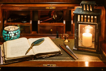 An open antique book in which a writing pen rests. are found on a wooden desk on leather. Two lighted lanterns are incorporated to illuminate with a candle
