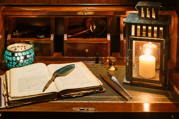 An open antique book in which a writing pen rests. are found on a wooden desk on leather. Two...