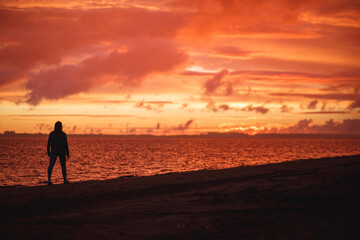 Woman walks alone on the beach and looks at the colorful sunset after the rain