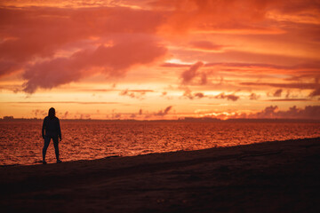 Obraz premium Woman walks alone on the beach and looks at the colorful sunset after the rain