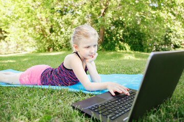 Caucasian girl child doing sport workout outdoor online. Video chat call with friends on Internet. Kid learning training on backyard with laptop. A new normal. Social distance at coronavirus.