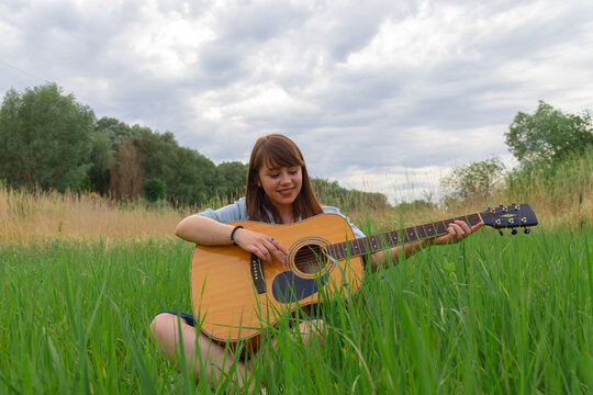 teenage girl portrait photography with acoustic guitar model posing outdoor green field peaceful summer June day time nature environment - Powered by Adobe