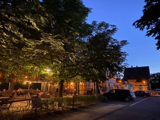 Biergarten unter Bäume, schöne Beleuchtung in den Bäumen befestigt Rechts Gebäude. 