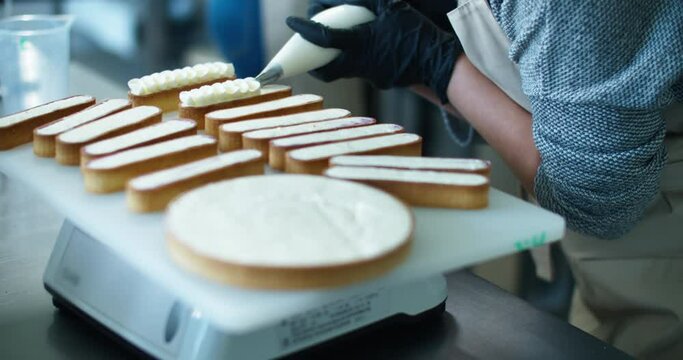 The woman's hands squeezing the cream on a cake and desserts. Tasty cream on the cake for sale