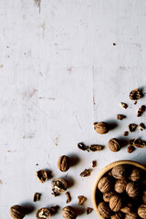 Walnut kernels in a wooden bowl and whole walnuts on a table. Walnuts