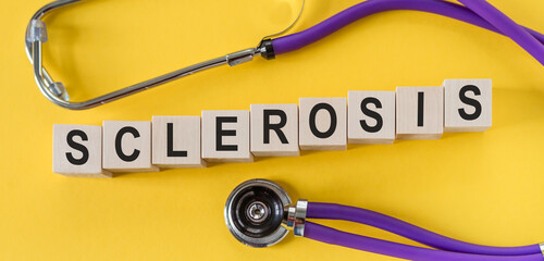 sclerosis word written in wooden blocks on yellow table with stethoscope. Medicine, health and wellbeing concept