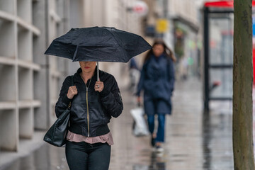 LONDON, ENGLAND - JUNE 10, 2020: Beautiful young woman caught out in the rain walking on a drizzly day under an umbrella in Holborn, London during the COVID-19 pandemic 119
