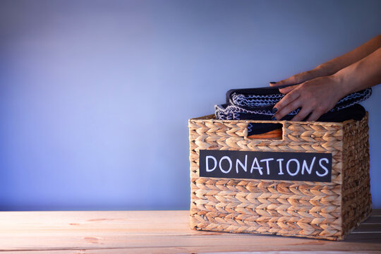 Hands Putting A Blanket In A Box For Clothing Donations On A Blue Background. Charity And Donation Concept. Copy Space.