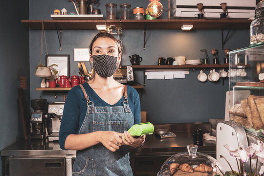 Caucasian woman handling card payment method in a small bakery business wearing mask durind covid-19 pandemic reopening after quarantine