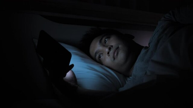 Asian male spending time with smartphone on the bed at night in home