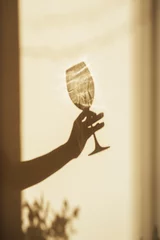 Tuinposter Shadow of a hand with a glass of wine on the light wall © valeriyakozoriz