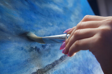 the hand of a female artist holds a brush. draws a close-up picture