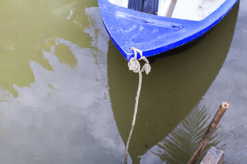 Small blue plastic rowboat on the water tied to a old wooden dock.