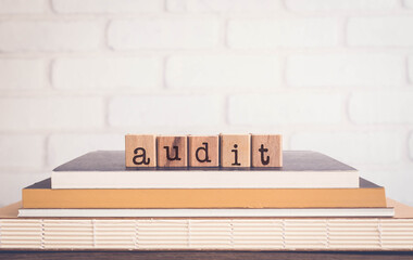 The word AUDIT, alphabets on wooden rubber stamps on top of books with bricks background, blank copy space, vintage minimal style. Concepts of examination, finance, accouting and business management.