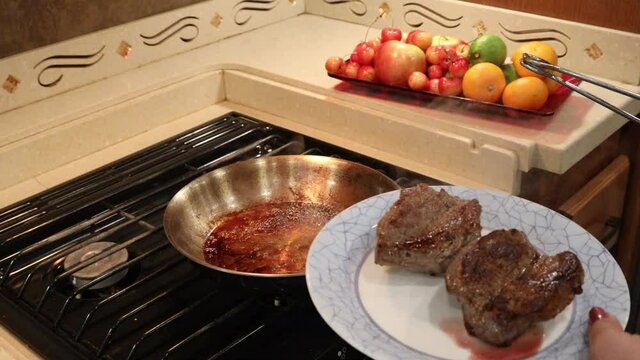 Woman removing cooked steaks from heated skillet and placing on plate