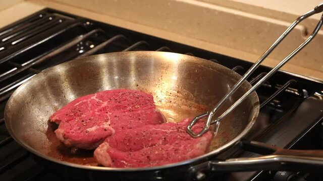 Woman laying butterflied and seasoned fillet steaks in melted butter in a hot stainless steel skillet