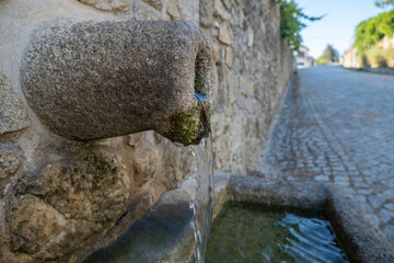 Fresh water flowing from old stone drinking water fountain in rural Portugal, close up.