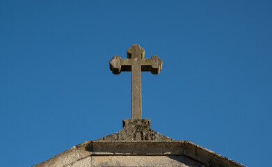 Old stone cross atop Catholic chapel in rural Portugal against blue sky.