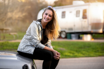 Smiling woman having fun camping outdoors with camper trailer RV, enjoying a fun experience outdoors