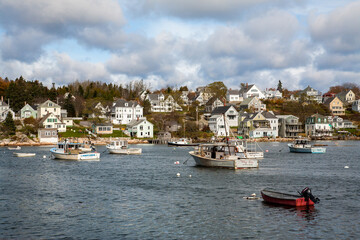 Fototapeta na wymiar Stongington, Maine; Lobster boats anchored in Stonington bay with New England style houses on the shore in the background.