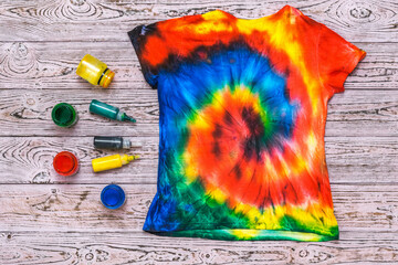The back of a tie dye t-shirt on a wooden table with paint. Flat lay.